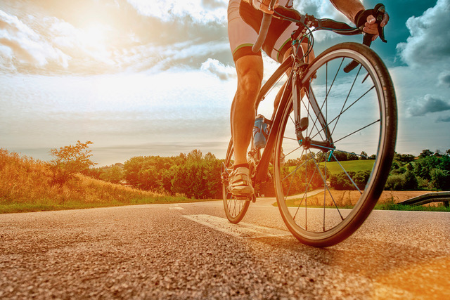 Close up of a athlete who rides his bike up a steep hill. The sun shines as his feet hits the pedals and he drives the bicycle forward.